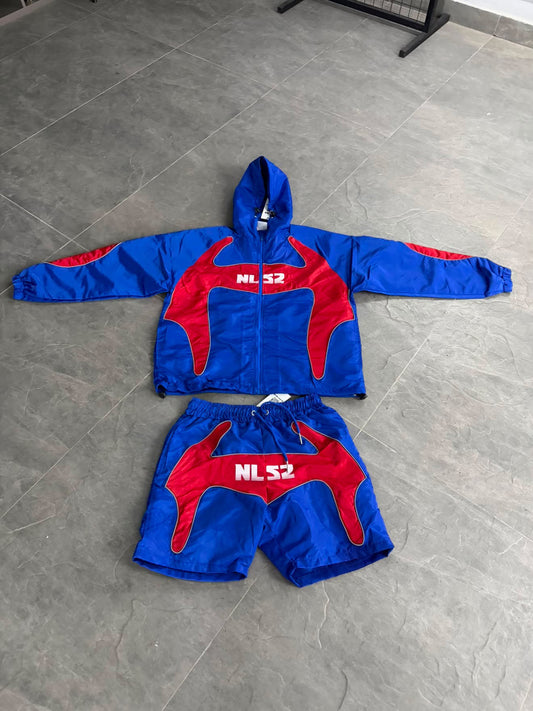 A two-piece set consisting of a hooded zip-up jacket and matching shorts, laid flat on a gray tiled floor. The set features a vibrant blue base with red graphic panels and white 'NLS2' lettering on the chest and shorts.
